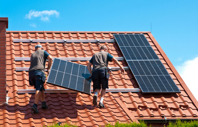 Deux installateurs en train de poser des panneaux solaires sur le toit d'une maison.