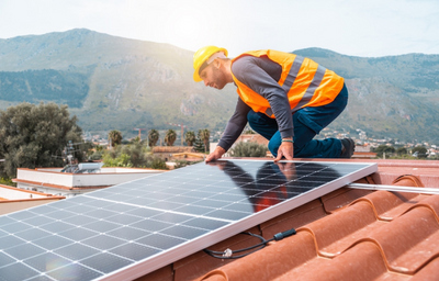 Ouvrier en train d'installer des panneaux solaires sur le toit d'une habitation.